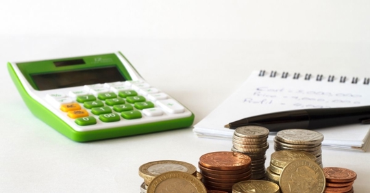 A calculator sitting near coins and a notebook