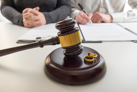 Two people sitting at table with paperwork behind gavel and rings.