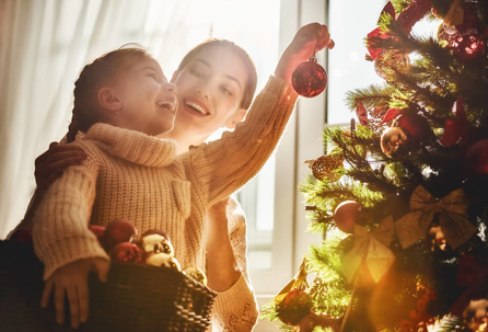 Mom and daughter decorate the Christmas tree indoors.